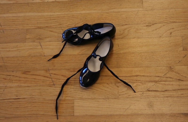 Black patent tap shoes with ribbon ties on a studio floor